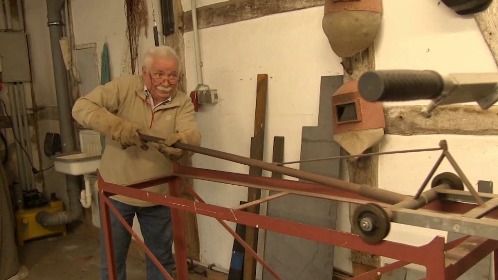 Helmut Senf in der Werkstatt bei der Arbeit mit einem Metallrohr zwischen den Händen..