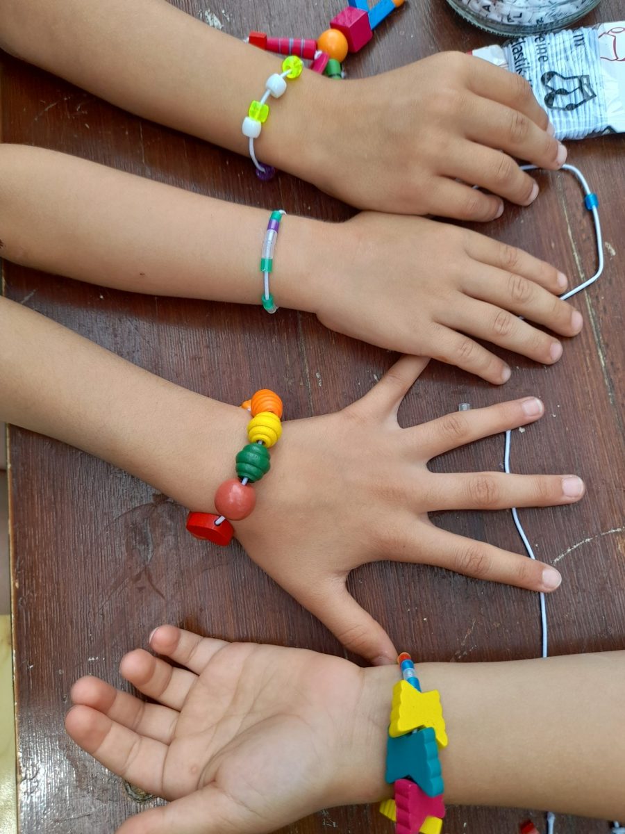 4 Kinderhände auf einem Tisch liegend mit bunten Armbändern.