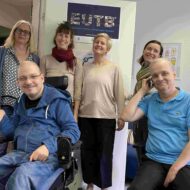 Ein Team-Foto der BZSL. Sechs Personen stehen zusammen im Büro. Vier Frauen stehen im Hintergrund, davor sitzen zwei Männer. Einer von ihnen sitzt in einem elektrischen Rollstuhl, der andere auf einem Schreibtischstuhl.