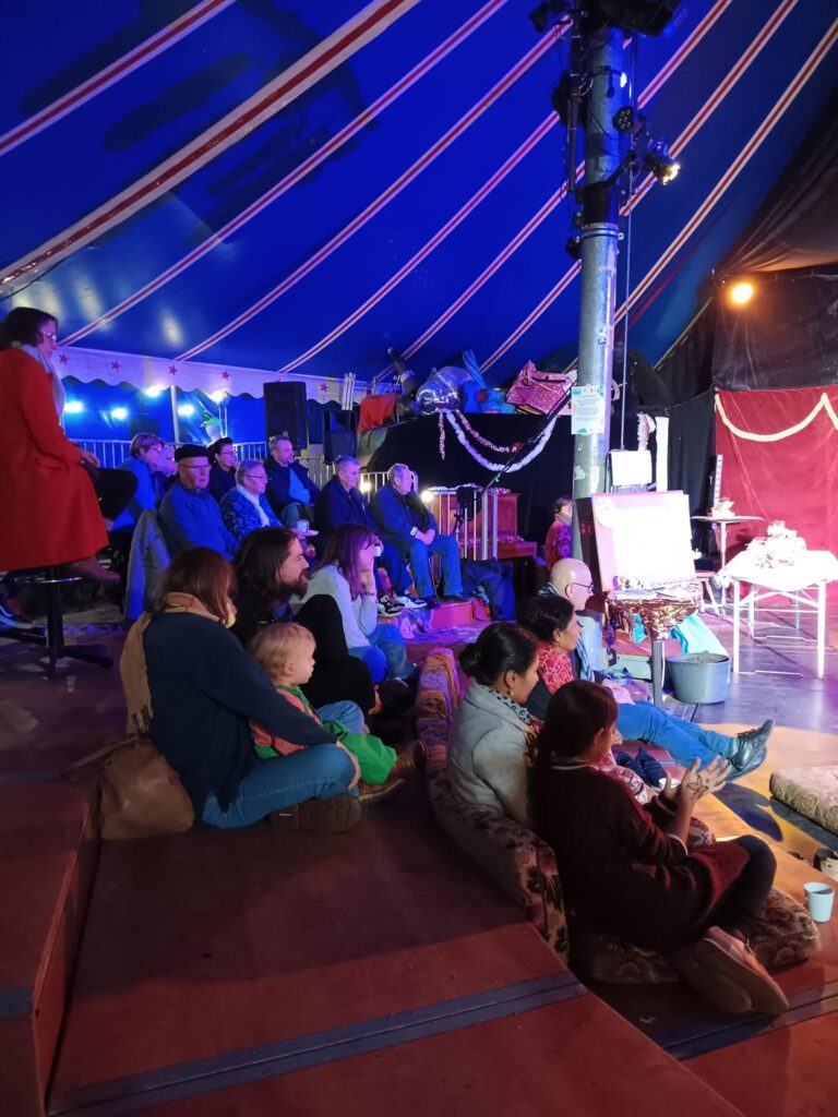 Junge Familien und ältere Menschen sitzen auf der Tribüne des Zirkus' und verfolgen eine Show.