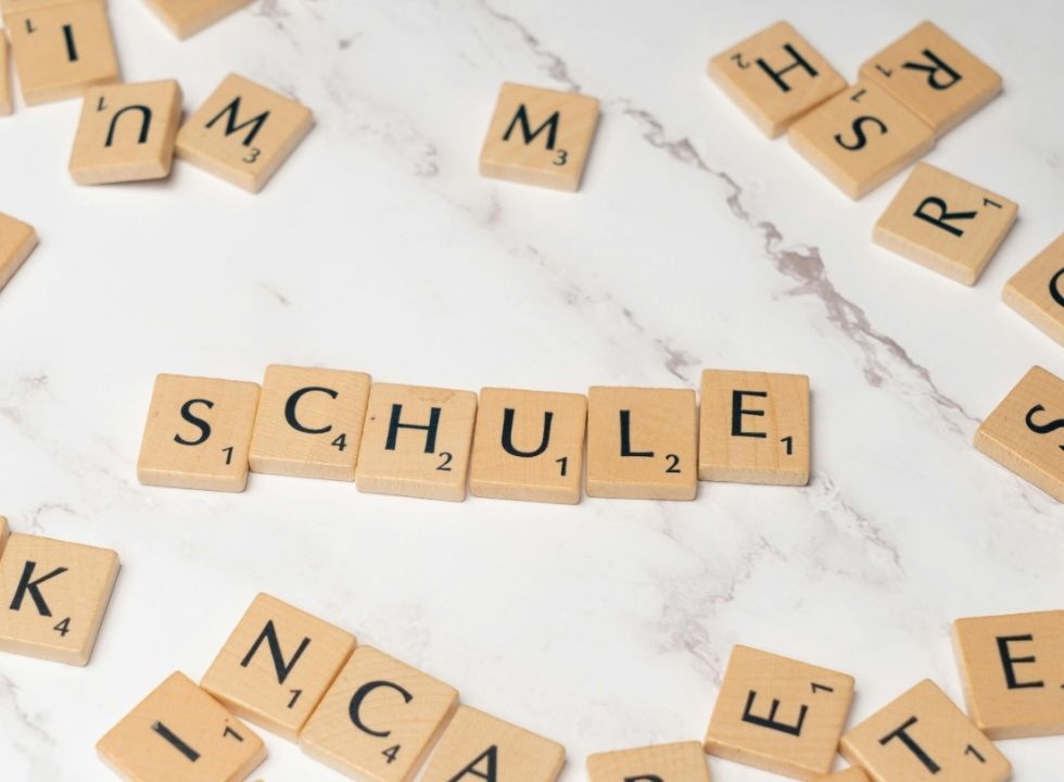 Durcheinander liegende Buchstaben aus einem Scrabble-Spiel. In der Mitte bilden mehrere Buchstaben das Wort "Schule".