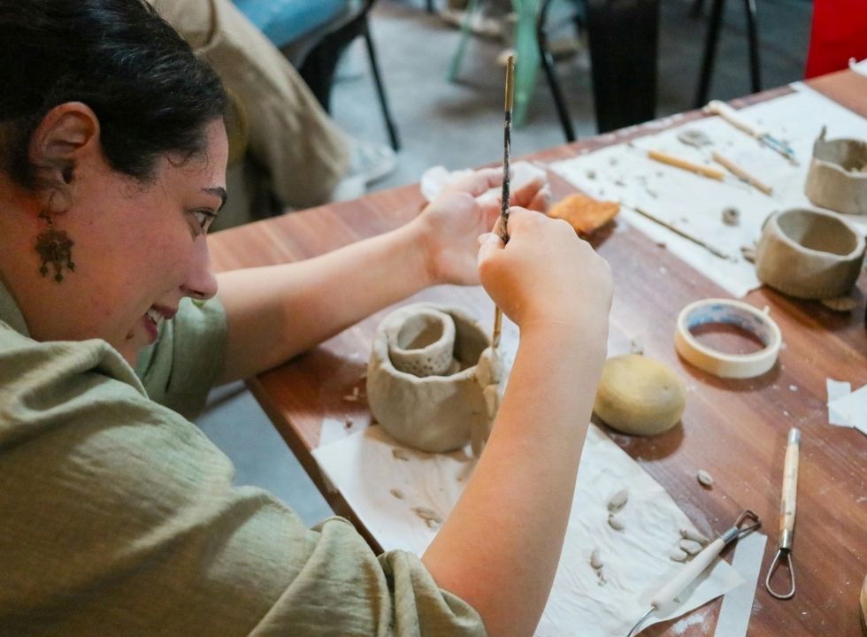 Das Bild zeigt eine Teenagerin, die mit einem Spatel ein Stück Ton bearbeitet. Sie lächelt und schaut konzentriert auf das Werkstück.